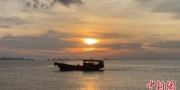 夕阳下，一艘渔船缓缓驶过水面。　张月和 摄 - 中新网海南频道